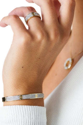 Close-up of a hand wearing a gold ring, bracelet, and earring on a white background